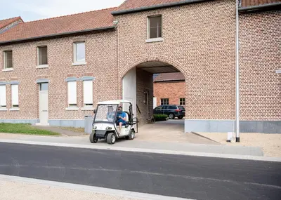 a person riding a golf cart in front of a brick building at B&B De Fruithoeve in Hoeselt