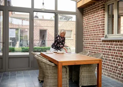 a woman sitting at a wooden table on a patio at B&B De Fruithoeve in Hoeselt
