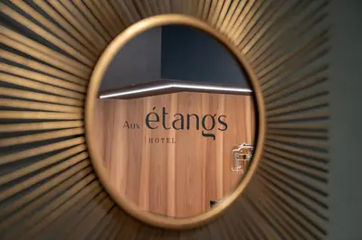 a round mirror with the name of anyamines hotel on a wall at Aux Etangs - Hôtel in Battice