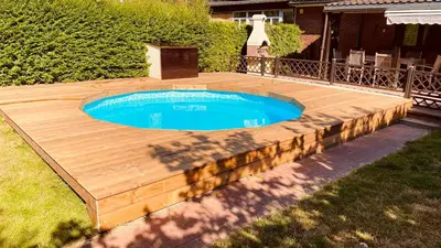 a wooden deck around a swimming pool in a yard at La douce Rive in Esneux