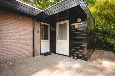 a black house with a white door and a brick building at Boshuisje Rekem - Rivus in Lanaken
