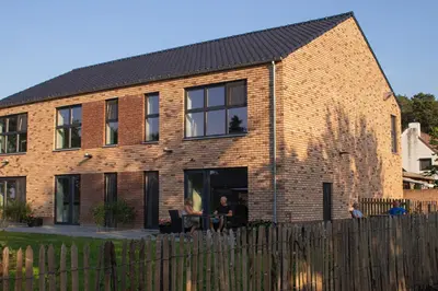 a brick house with a man sitting in the doorway at De Hoog Velden 12 in Pelt