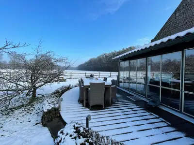a deck with a table and chairs in the snow at B&B De Paenhoeve in Eksel